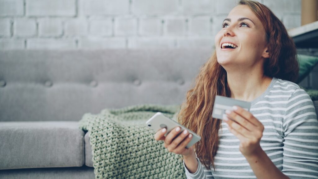 A happy woman holding a credit card and smartphone.