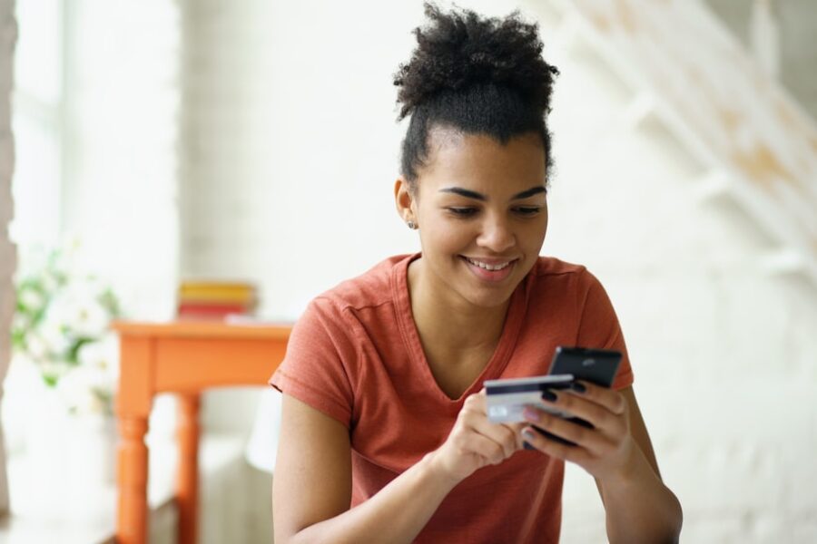 Young woman smiling while holding credit card and phone