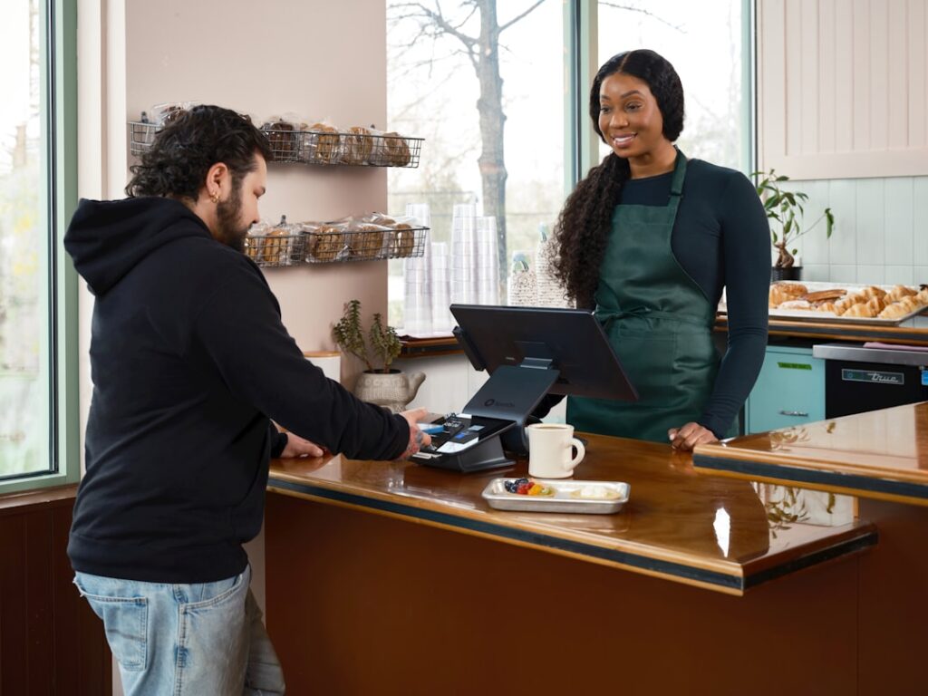 A man pays a smiling woman at a cafe counter.