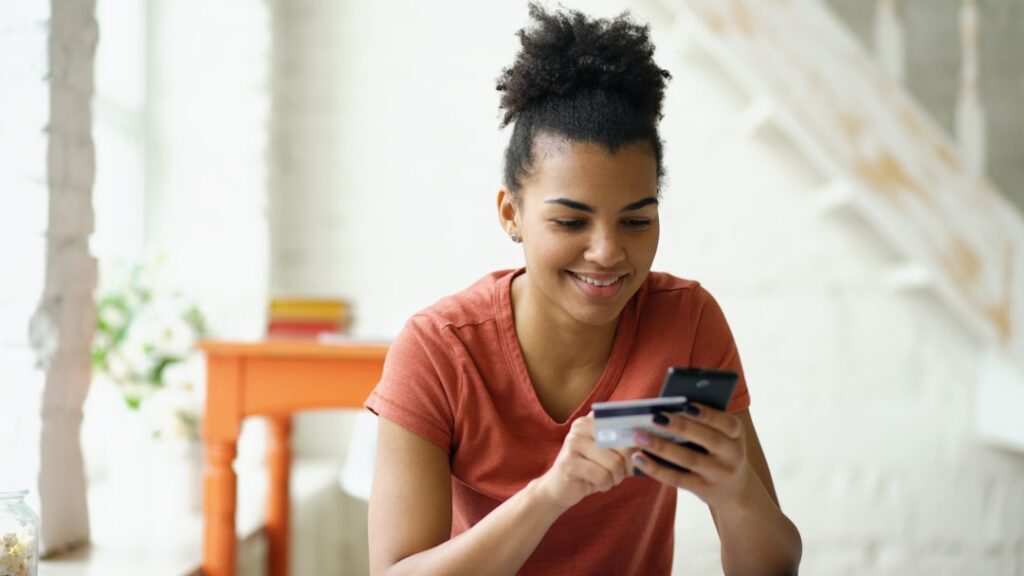 Young woman smiling while holding credit card and phone